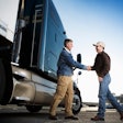 A customer shakes hands with a salesperson in front of a tractor trailer.