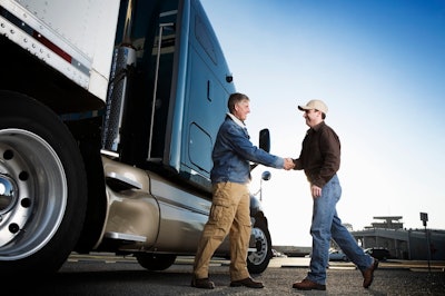 A customer shakes hands with a salesperson in front of a tractor trailer.