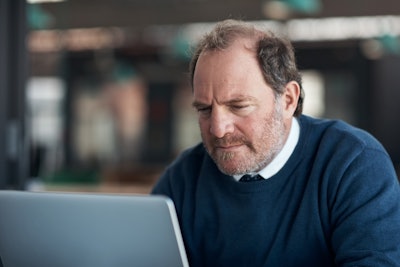 Man in blue sweater looks at laptop computer