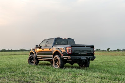 black Hennessey 2024 Ford F-150 Velociraptor rear side view in green meadow