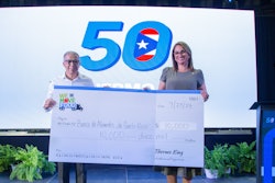 Two people hold a large check for $10,000 in front of a screen.