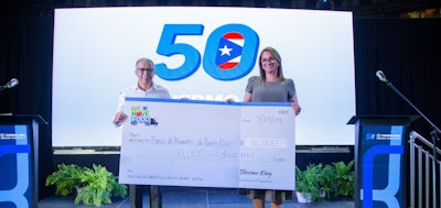 Two people hold a large check for $10,000 in front of a screen.