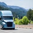 A blue truck hauling a trailer with forested mountains in the background