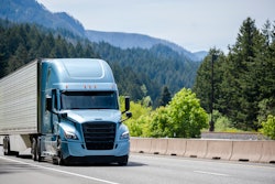 A blue truck hauling a trailer with forested mountains in the background