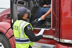 An enforcement officer hands documentation back to a driver in the seat of a Class 8 truck.