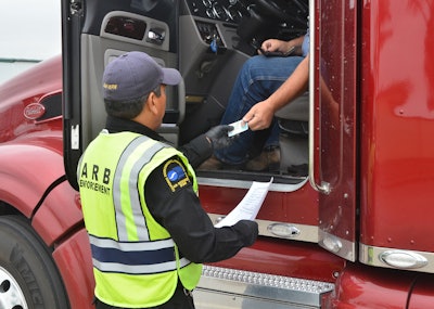 An enforcement officer hands documentation back to a driver in the seat of a Class 8 truck.