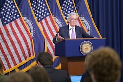 A man speaks at a podium in front of flags.