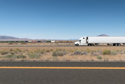 A truck and trailer drives on a highway in the desert.