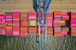 A ship full of multicolored cargo containers is moored under a blue crane at the port of Jacksonville, Florida.