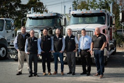 A group of men standing in front of trucks on a lot.
