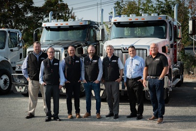 A group of men standing in front of trucks on a lot.