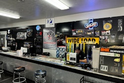 A man works behind a counter with a computer and signage