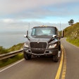 An electric International truck drives on a coastal road.