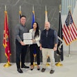 Three people in front of flags holding an award