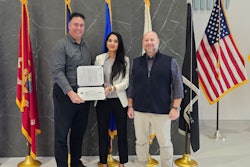Three people in front of flags holding an award