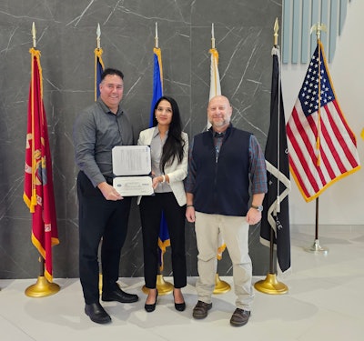 Three people in front of flags holding an award