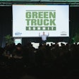 A man speaks on stage in front of a screen that reads Green Truck Summit