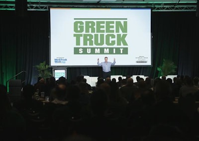 A man speaks on stage in front of a screen that reads Green Truck Summit