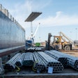 Cranes unload pipe from a ship at a port