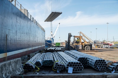 Cranes unload pipe from a ship at a port
