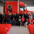 A group of people pose in front of a red truck hung with a holiday wreath.