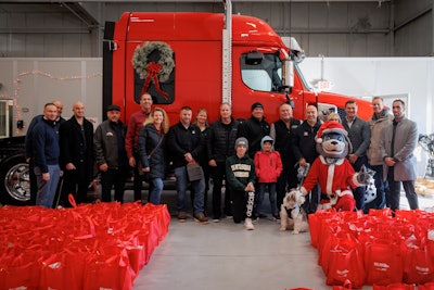 A group of people pose in front of a red truck hung with a holiday wreath.