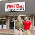 Two men stand in front of a building that says First Call Truck Parts
