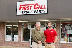 Two men stand in front of a building that says First Call Truck Parts