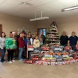 A group of people stand with a pile of toy trucks in front of a Christmas tree.