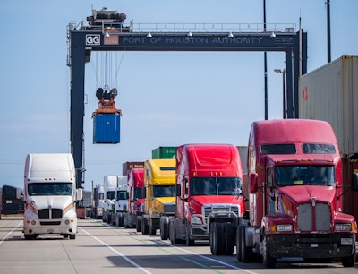 A line of trucks under a crane at a port.
