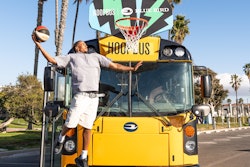 A man dunking a basketball in a hoop attached to an electric school bus from Blue Bird.