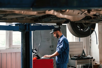 A man works on a laptop under a vehicle.
