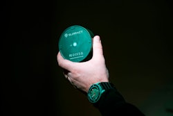 A hand holding a Surfact Emma tracker the shape and size of a hockey puck.