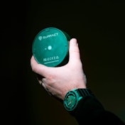 A hand holding a Surfact Emma tracker the shape and size of a hockey puck.