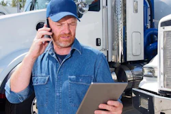 A man on the phone holding a tablet stands in front of trucks.