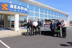 A group of people stand in front of a work truck in front of a Reading Truck building