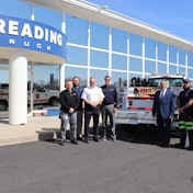 A group of people stand in front of a work truck in front of a Reading Truck building