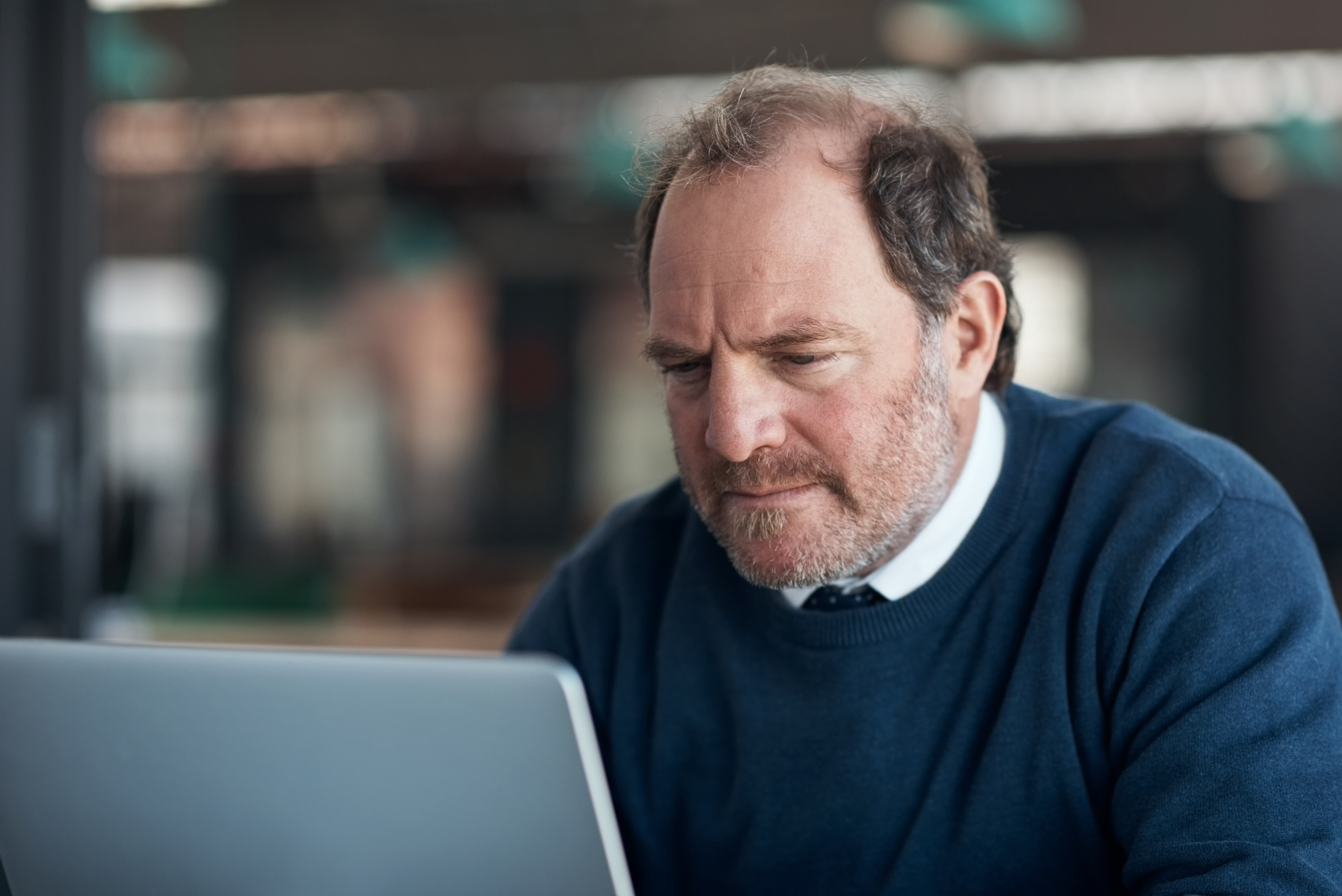 Man In Blue Sweater Looks At Laptop Computer