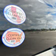 Two 'Certified Clean Idle' oval stickers on vehicle window with cloudy sky background