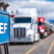 DEF fuel sign at truck stop with semi-trucks parked in background on highway