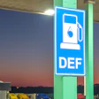 Blue DEF fuel pump sign with water droplet icon mounted on green pole at dusk