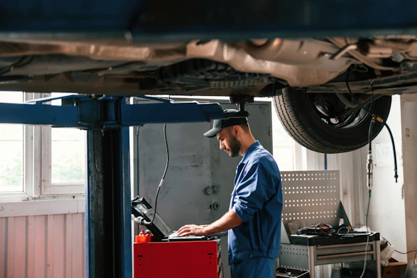 Male Tech Under A Vehicle With Laptop