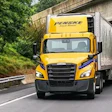 Yellow Penske moving truck driving on highway under concrete overpass with green foliage