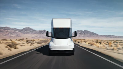 A front-facing view of a white Tesla Semi driving along a desert highway.