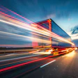 Semi-truck speeding on highway at sunset with motion blur effect and glowing red taillights