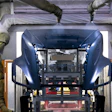 Dark blue vehicle in industrial paint spray booth with protective coverings and overhead equipment