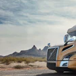 Gold Volvo semi-truck parked in desert landscape with rocky mountains in background