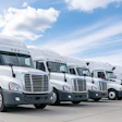 Fleet of white commercial semi-trucks lined up in a row under blue sky