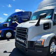 White and blue Mack commercial trucks parked in a lot under clear sky