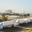 Fleet of commercial trucks parked in industrial yard with warehouses and mountains in background